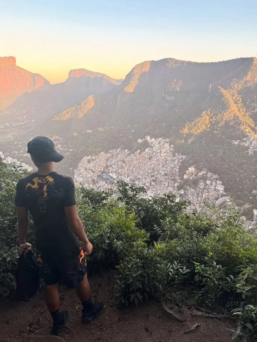 A hiker looking out over the Rocinha favela from a mountaintop viewpoint at sunrise