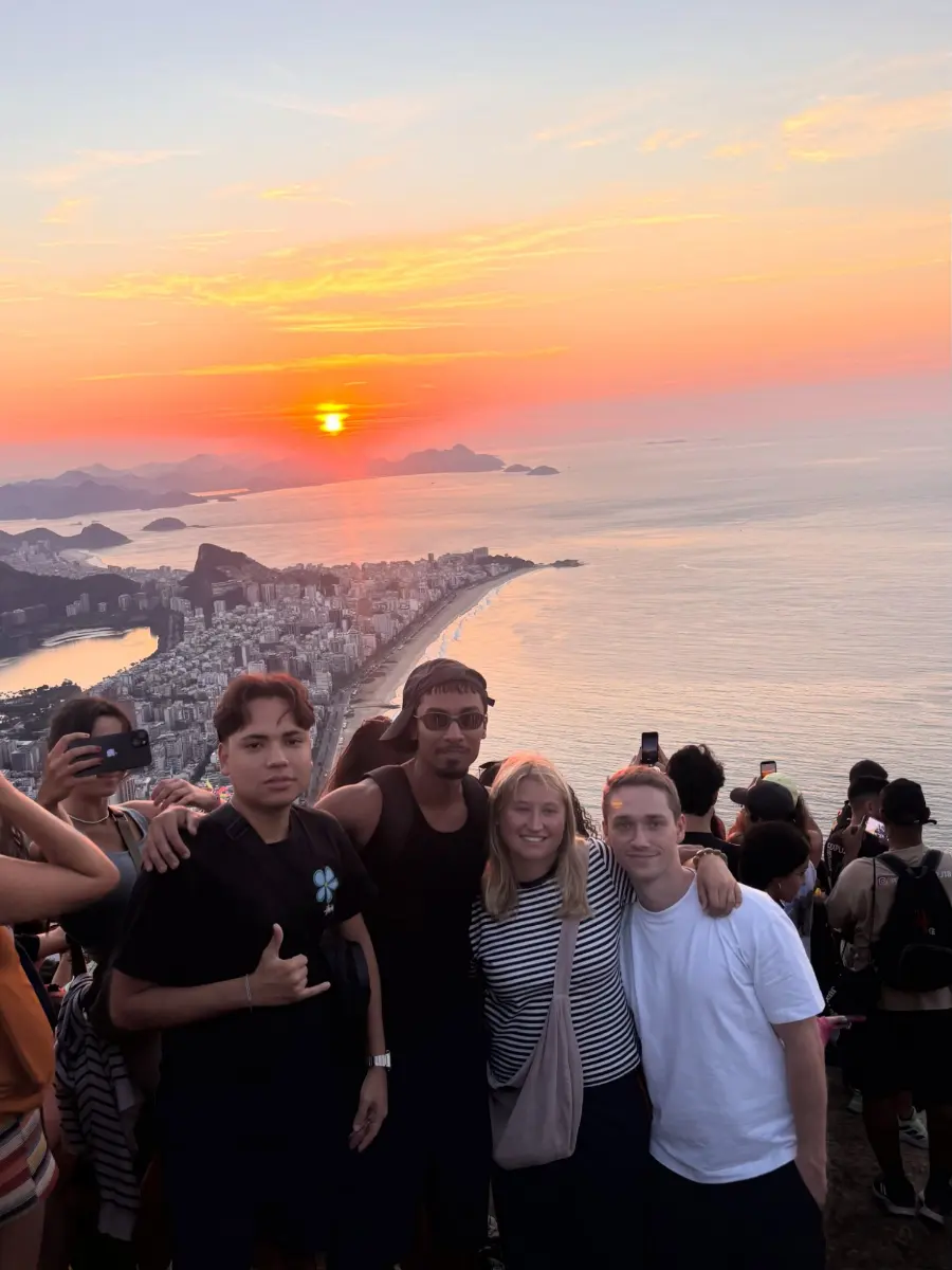 Travellers and their guide at the summit of Dois Irmaos as the sun rises over the ocean beyond Ipanema