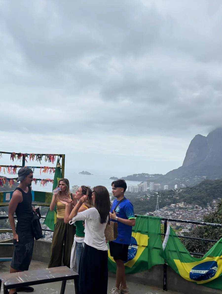 The group at a viewpoint hung with Brazilian flags and ribbon ties, Rocinha spilling down the hillside behind them and the ocean beyond